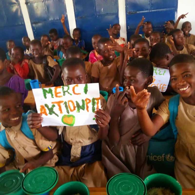 Kinder in Togo halten lachend ein selbstgemaltes Schild mit der Aufschrift „Merci Aktion PiT“ hoch